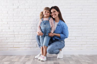 Güzel anne ve küçük kızı beyaz tuğla duvarın yanında