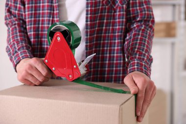 Karton kutuyu kapalı bir yere kapatmak için yapıştırıcılı bant kullanan bir adam.