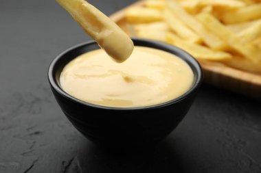 Patates kızartmasını siyah masada peynir sosuna batırmak, yakın plan.