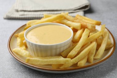 Lezzetli peynir sosu kasede ve patates kızartması gri masada, yakın plan.