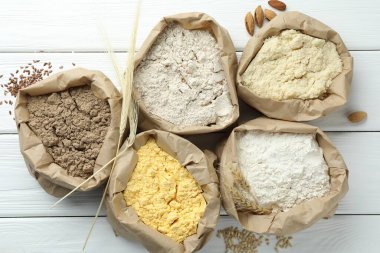 Beyaz ahşap masa üzerinde kağıt torbalarda farklı türde un, düz yerde.