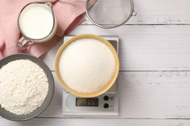 Dijital mutfak terazisi, bir kase şeker ve beyaz ahşap masa üzerindeki diğer ürünler, düz yatak. Metin için boşluk