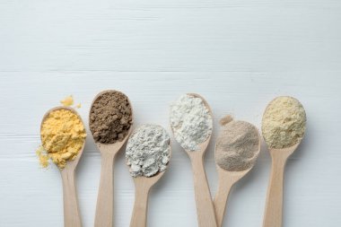 Beyaz ahşap masadaki kaşıklarda farklı türde un, düz. Metin için boşluk