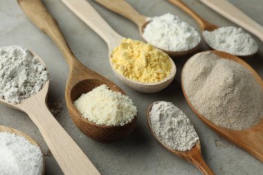 Açık gri masada kaşıklarda farklı türde un, yakın plan.