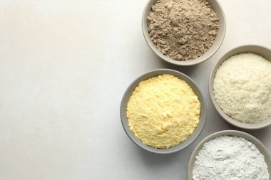 Açık gri masadaki kaselerdeki farklı un türleri, düz yatış. Metin için boşluk