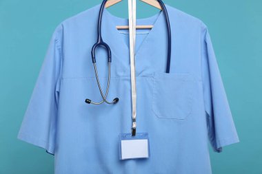 Steteskop ve rozetli sağlık çalışanı üniforması mavi arka planda.