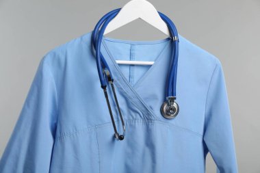 Steteskoplu sağlık çalışanı üniforması gri arka planda, yakın plan.