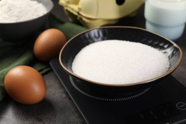 Gri masadaki şeker ve diğer ürünlerle birlikte dijital mutfak terazisi, yakın plan.