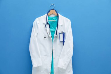 Steteskop ve rozetli doktorun ceketi mavi arka planda asılı.