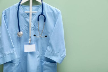 Steteskop ve rozeti açık yeşil arka planda asılı sağlık görevlisi üniforması. Metin için boşluk