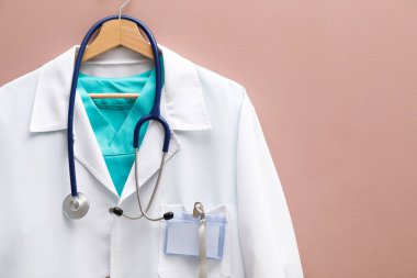Doktor ceketi, steteskop ve rozeti bej arka planda asılı. Metin için boşluk