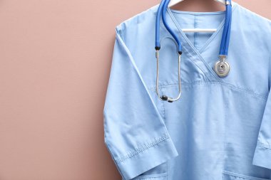 Bej arka planda steteskop takılı sağlık çalışanı üniforması. Metin için boşluk