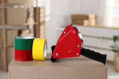 Kapalı alandaki karton kutunun üzerinde yapışkan bant ruloları olan bir dağıtıcı.