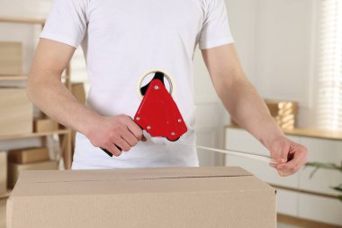 Karton kutuyu kapalı bir yere kapatmak için yapıştırıcılı bant kullanan bir adam.