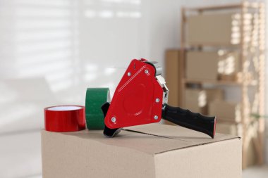 Kapalı alandaki karton kutunun üzerinde yapışkan bant ruloları olan bir dağıtıcı.