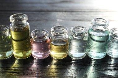 Siyah ahşap arka planda aromatik yağlı parfüm şişeleri, yakın plan.