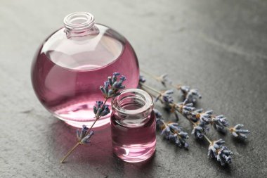 Açık parfüm şişeleri aromatik esanslı yağlar ve lavanta dalları koyu dokulu masa, yakın çekim