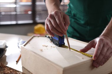 İçerideki masada bant ve kalemle ahşap kutuyu ölçen adam, yakın plan.