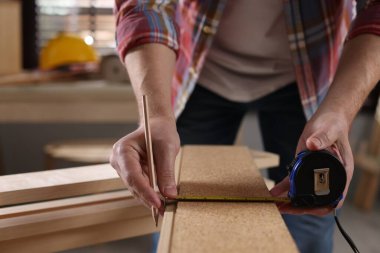 Kapalı mekanda tahta bant ve kalemle tahta ölçen bir adam var.