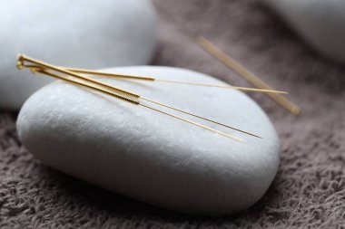 Akupunktur iğneleri ve spa taşları kahverengi havluda, yakın plan.