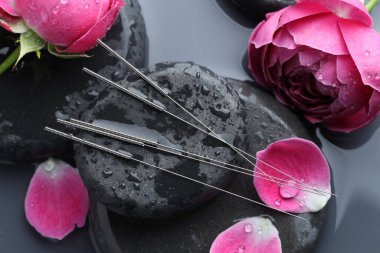 Akupunktur iğneleri, spa taşları ve çiçekler gri arka planda, üst manzara