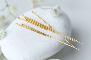 Akupunktur iğneleri, çakıl taşı taşı ve çiçekler ışık masasında, yakın plan.