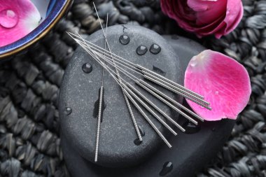 Akupunktur iğneleri, ıslak spa taşları hasır hasırın üzerinde çiçekler, düz uzanmış