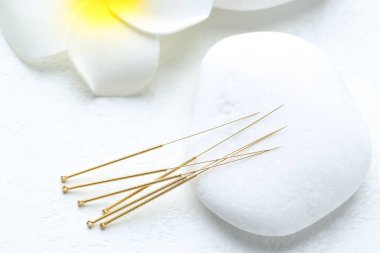 Beyaz arka planda akupunktur iğneleri, spa taşı ve çiçek, yakın plan.