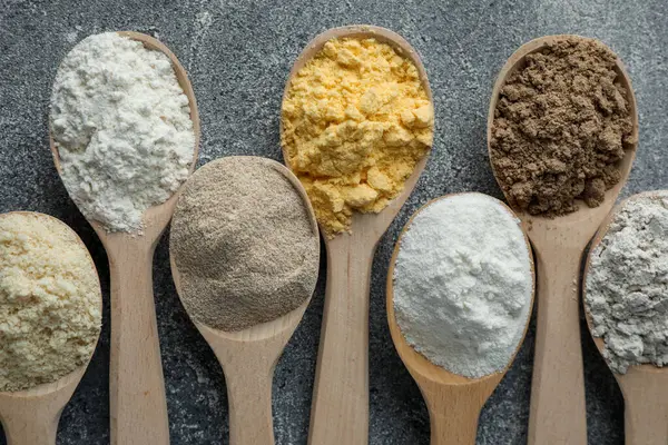 Gri masadaki kaşıklarda farklı türde un, düz.