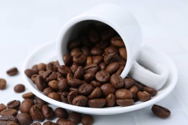 Aromatik kahve çekirdekleri, fincan ve çay tabağı beyaz masada, yakın plan.