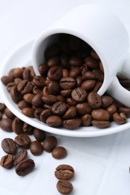 Aromatik kahve çekirdekleri, fincan ve çay tabağı beyaz masada, yakın plan.