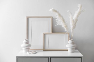 Beyaz duvarın yanındaki dolapta boş resim çerçeveleri ve şık ev dekorasyonu