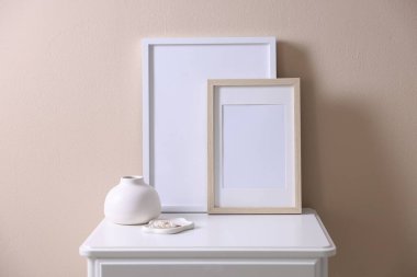 Boş resim çerçeveleri, vazo ve mücevherler bej duvarın yanındaki dolapta.