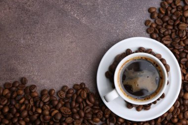 Aromatik kahve fincanda, fincan tabağı ve kahve çekirdekleri kahverengi desenli masada, düz yerde. Metin için boşluk