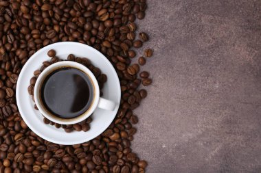 Aromatik kahve fincanda, fincan tabağı ve kahve çekirdekleri kahverengi desenli masada, düz yerde. Metin için boşluk