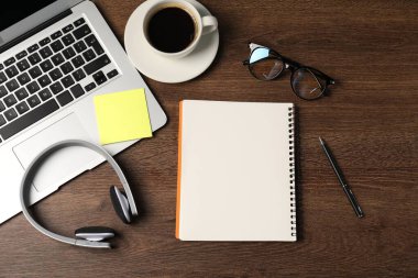 Not defteri, yapışkan not, kalem, kulaklık, kahve ve dizüstü bilgisayar ahşap masaya, düz uzan.