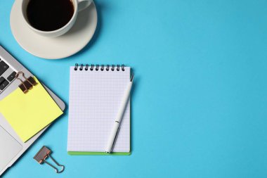 Not defteri, yapışkan not, kalem, cilt klipleri, açık mavi arka planda kahve ve dizüstü bilgisayar, düz. Metin için boşluk