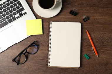 Not defteri, kalem, yapışkan not, cilt klipsleri, bardaklar, kahve ve dizüstü bilgisayar ahşap masa, düz uzanma