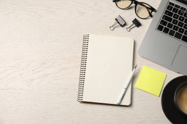 Not defteri, kalem, yapışkan not, cilt klipsleri, bardaklar, kahve ve dizüstü bilgisayar beyaz ahşap masa, düz yatak. Metin için boşluk