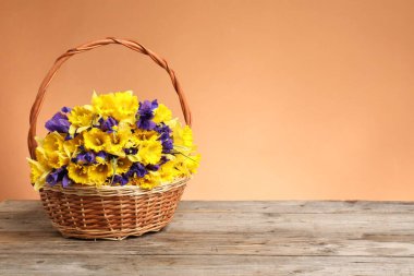 Mercan zeminine karşı ahşap masanın üzerinde güzel çiçekler olan hasır sepet. Metin için boşluk