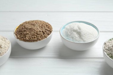 Beyaz ahşap masadaki kaselerdeki farklı un türleri, yakın plan.