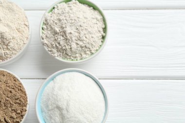 Beyaz ahşap masadaki kaselerdeki farklı un türleri, düz yatış. Metin için boşluk