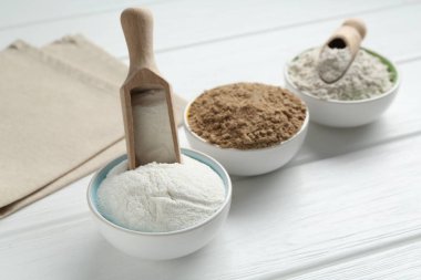 Kâselerdeki farklı un türleri ve beyaz ahşap masadaki kepçeler, yakın plan.