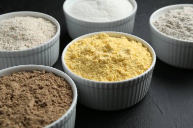 Siyah desenli masa üzerindeki kaselerde farklı un türleri, yakın plan.