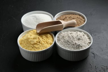 Kâselerdeki farklı un türleri ve siyah desenli masaya kepçe, yakın plan.