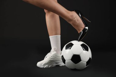 Arka planda futbol topu olan yüksek topuklu ayakkabılı ve spor ayakkabılı bir kadın.