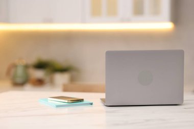 Dizüstü bilgisayar, akıllı telefon ve defter mutfaktaki beyaz mermer masada.