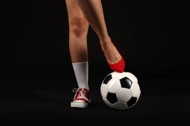 Arka planda futbol topu olan yüksek topuklu ayakkabılı ve spor ayakkabılı bir kadın.