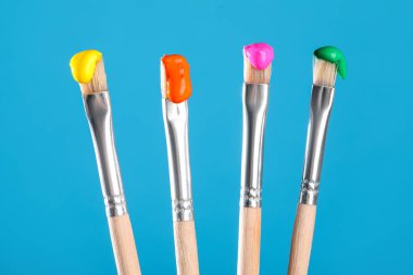 Açık mavi arkaplanda renk boyalı birçok fırça, yakın plan