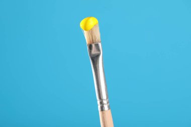 Açık mavi arkaplanda sarı boyalı fırça, yakın plan